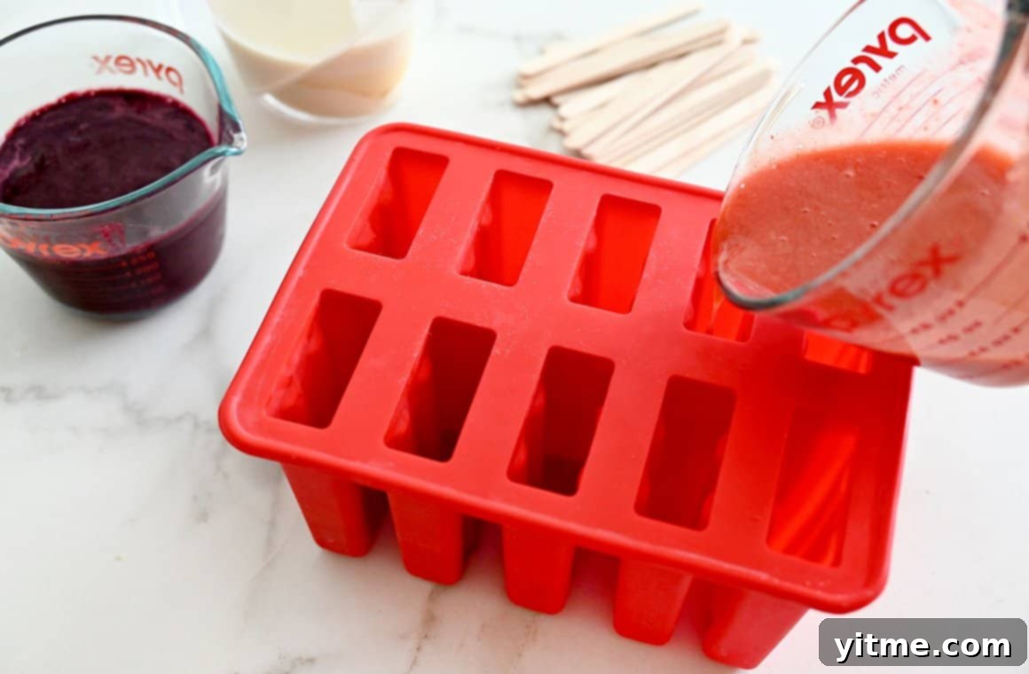 Strawberry puree being poured into a red popsicle mold