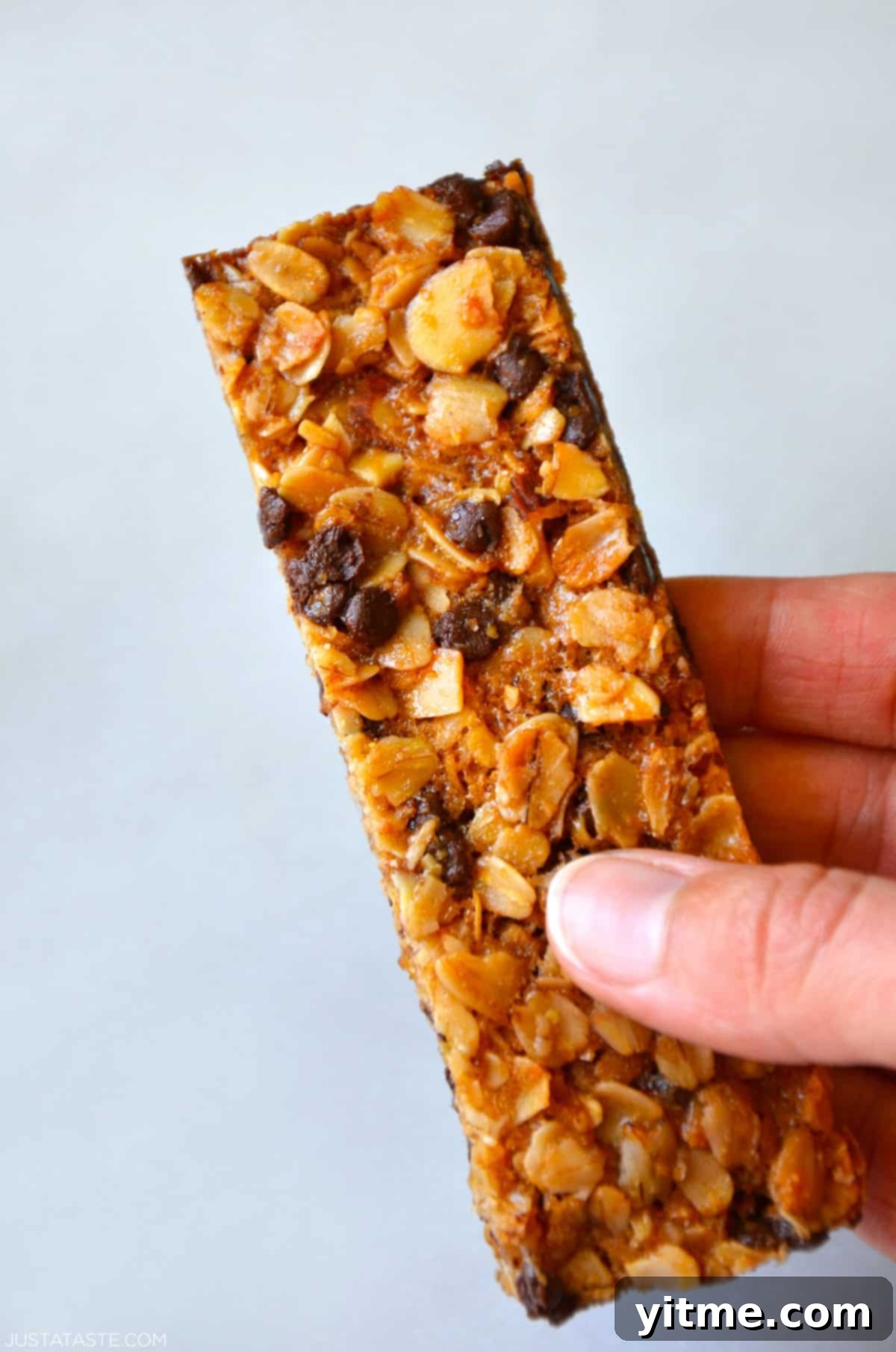 Close-up of a soft and chewy homemade chocolate chip granola bar being held in a hand.