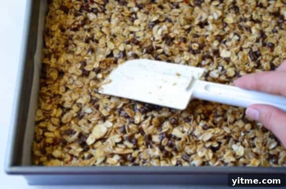 A person using a spatula to press a granola mixture evenly into a baking pan.
