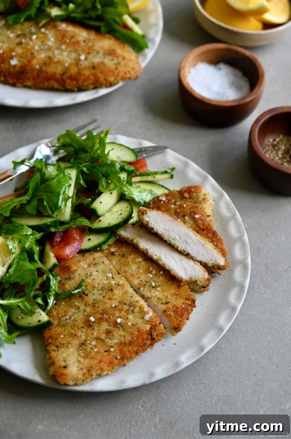 Crispy, golden brown Wiener schnitzel on a white dinner plate with a simple green salad.