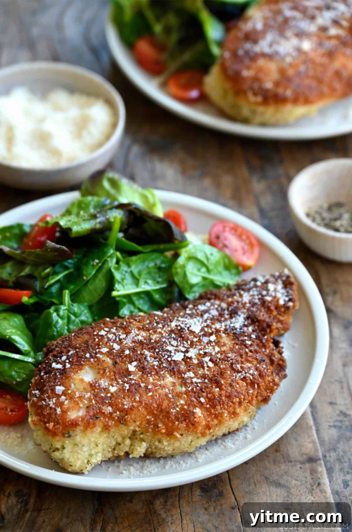 Parmesan herb crusted chicken breast on a plate with a simple Romaine and cherry tomato salad.