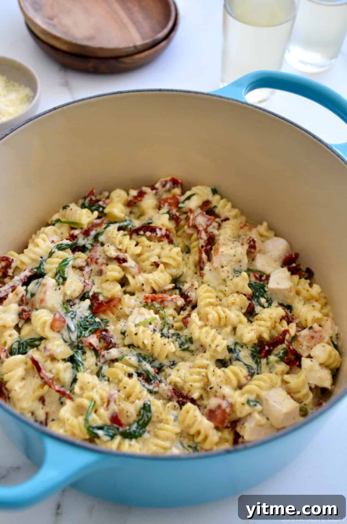 Creamy Tuscan pasta with diced chicken breasts, sun-dried tomatoes and spinach in a Dutch oven next to a small bowl containing Parmesan cheese.