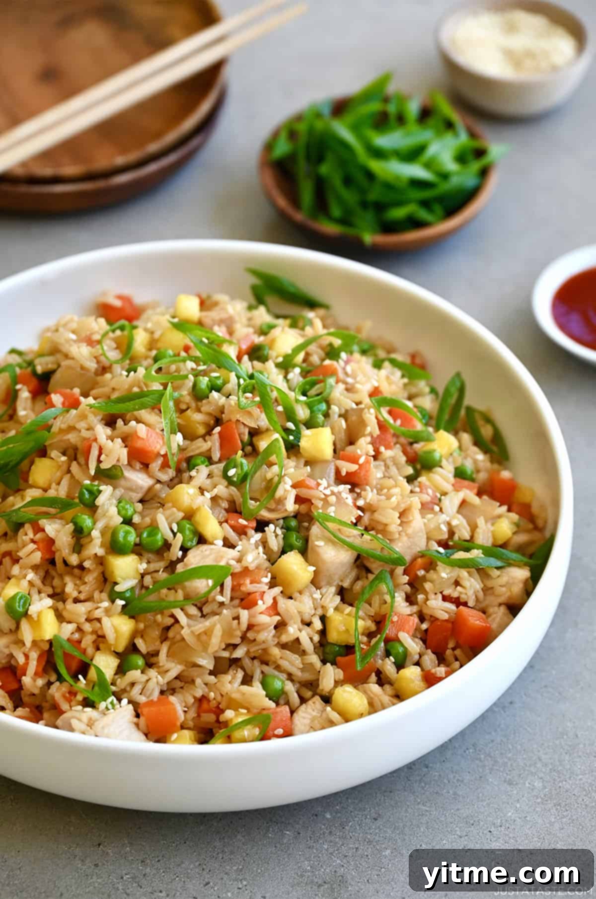 Pineapple chicken fried rice in a white bowl next to a small bowl filled with sliced scallions.