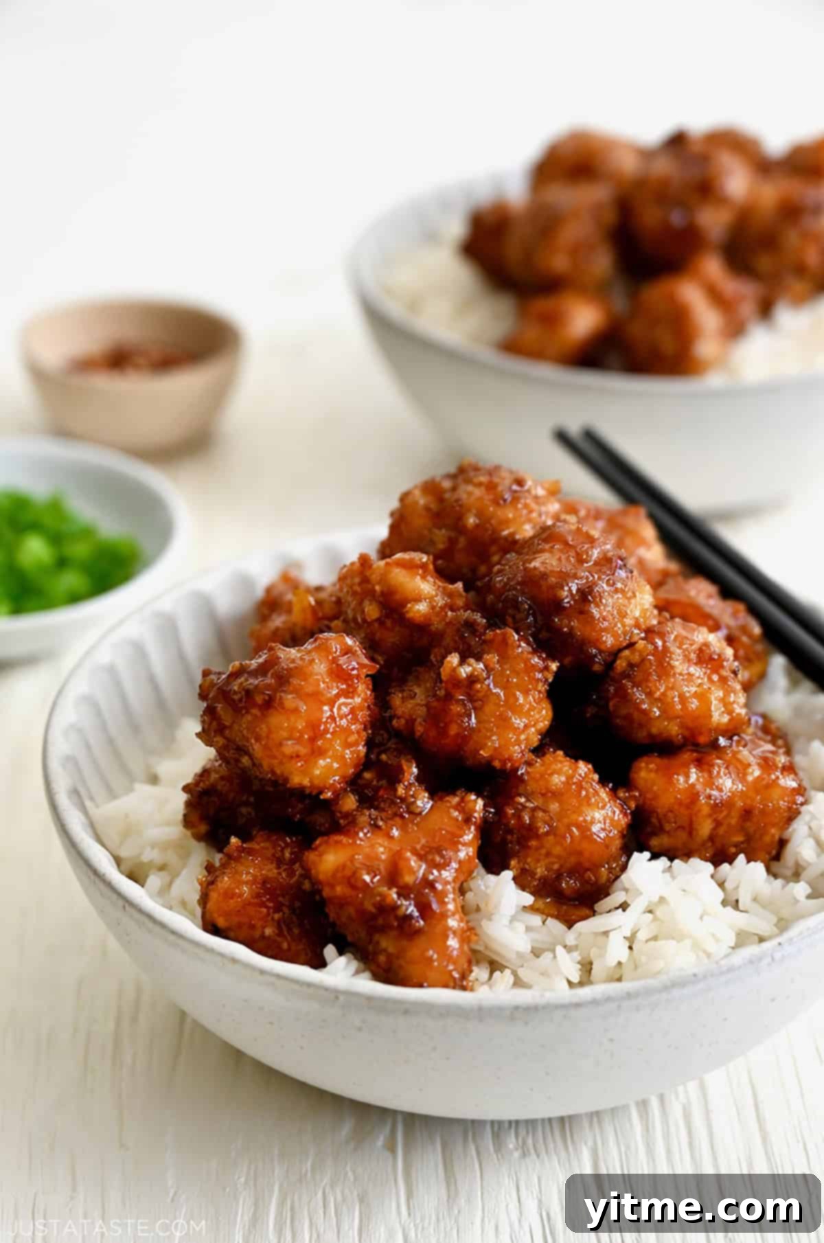 Baked Orange Chicken atop white rice in a bowl with chopsticks.