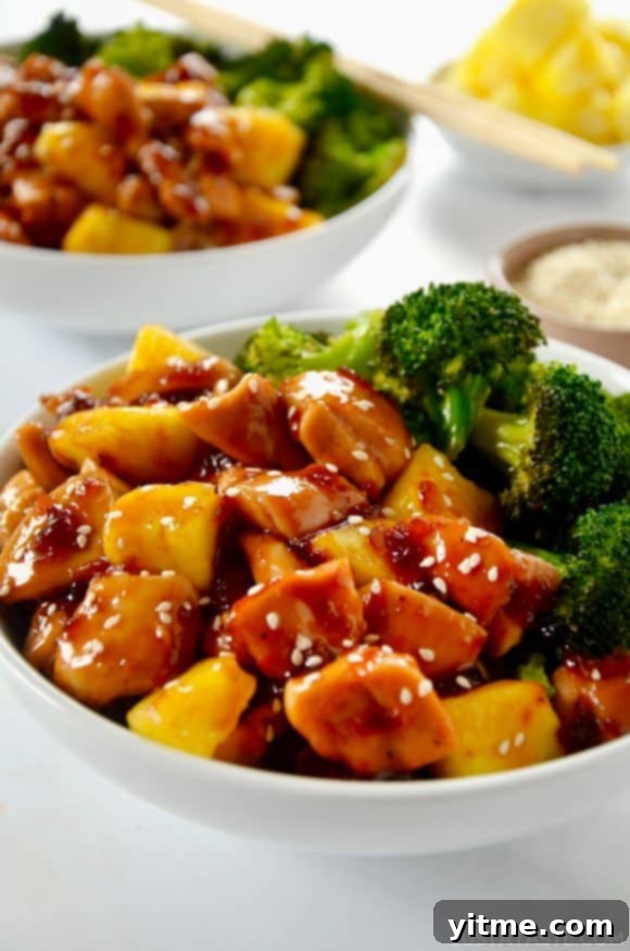 White bowl containing Sheet Pan Pineapple Chicken and Broccoli garnished with sesame seeds