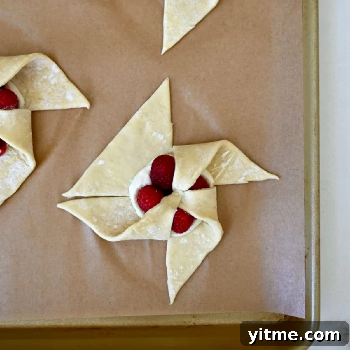 Step 3 of shaping a pinwheel: Continuing the process by folding a third puff pastry corner into the center, building the spiral.