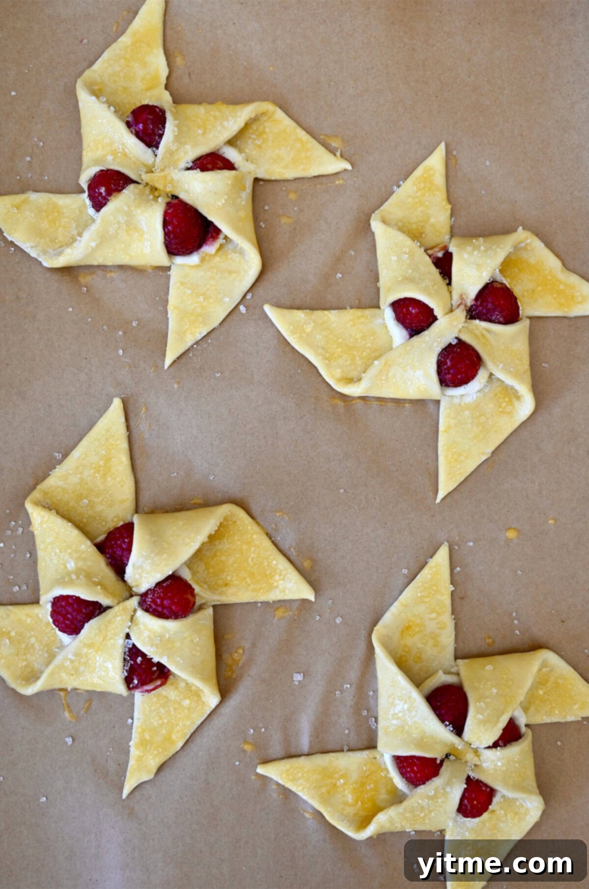 Pinwheel pastries, perfectly shaped, brushed with egg wash, and glistening with sanding sugar, ready for baking on a parchment-lined baking sheet.