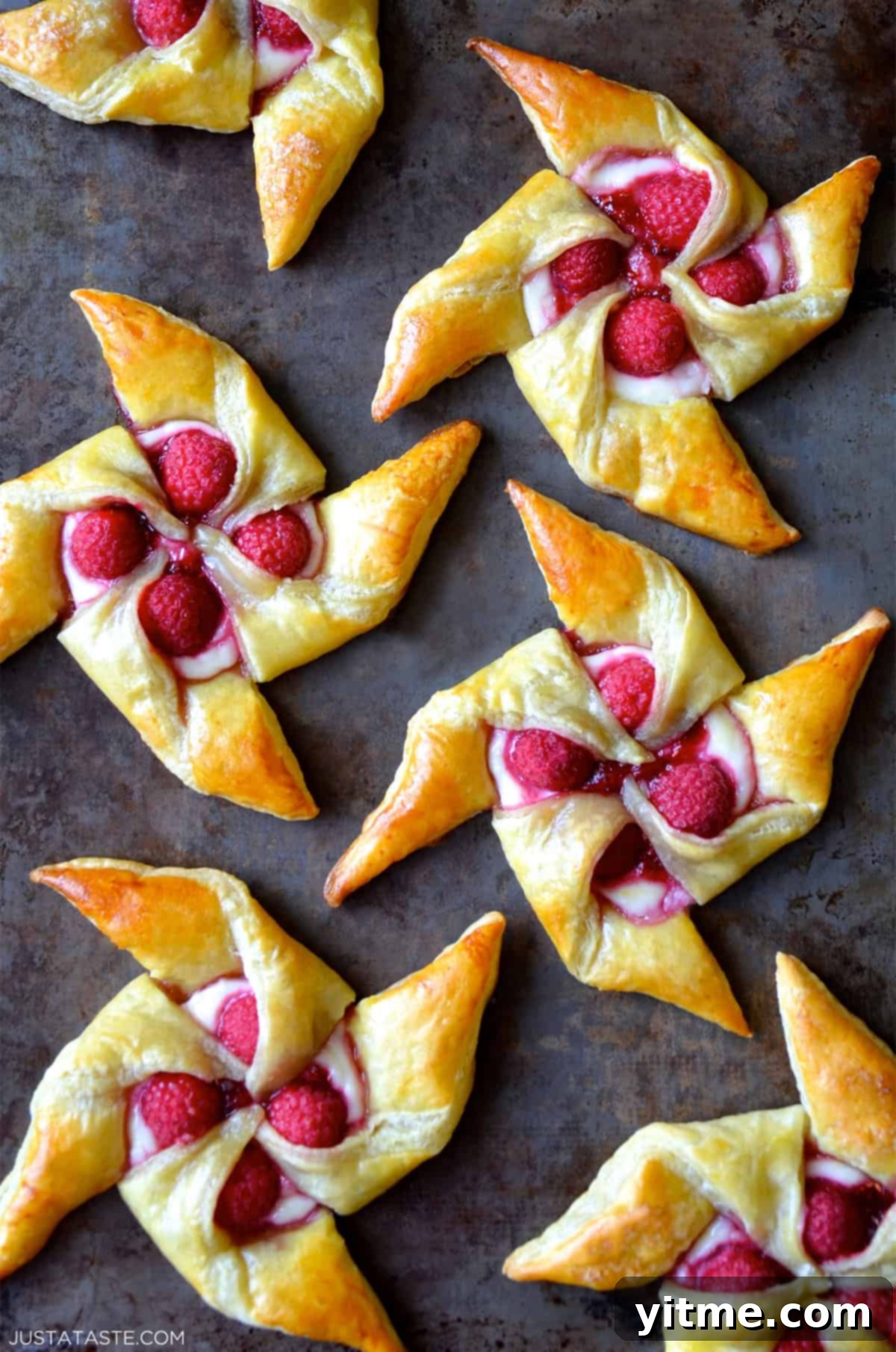 Raspberry cream cheese pinwheel pastries on a dark marble countertop, garnished with fresh raspberries and a dusting of powdered sugar.