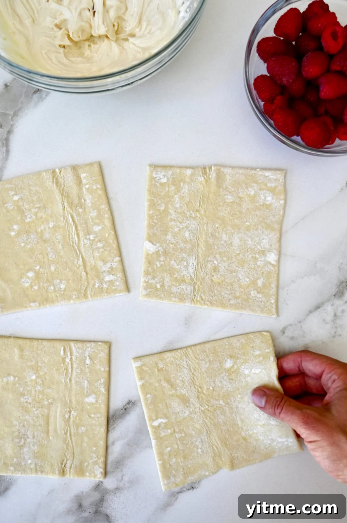 Thawed puff pastry sheets rolled out and cut into even squares on a lightly floured marble surface, ready for filling.