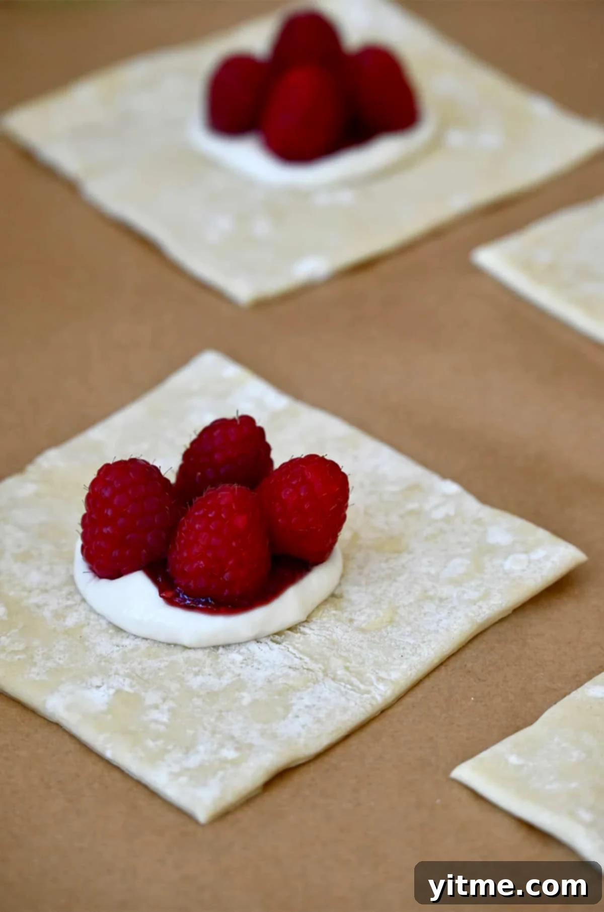 A puff pastry square, now layered with cream cheese, raspberry jam, and four plump fresh raspberries in the center.