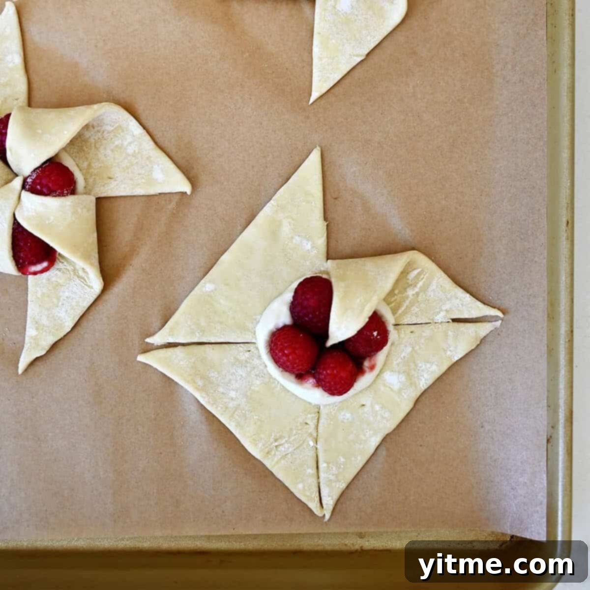 Step 1 of shaping a pinwheel: Gently folding one corner of a cut puff pastry section towards the center over the filling.