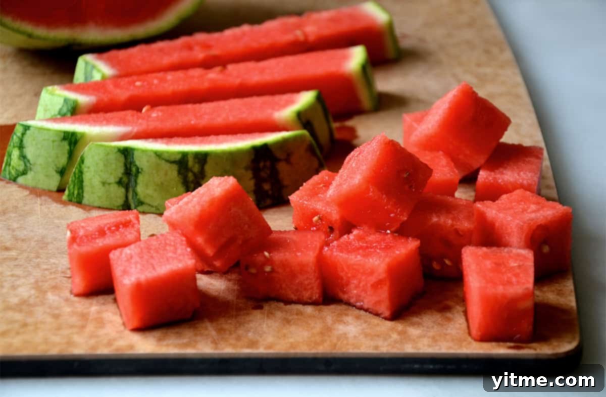 Cubed watermelon next to the rind on a wood cutting board.