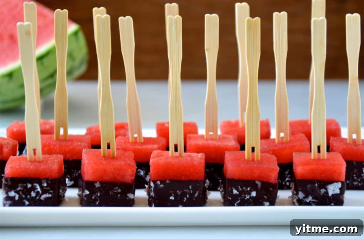 Perfect rows of watermelon bites dipped in chocolate and sprinkled with sea salt on a white serving platter.
