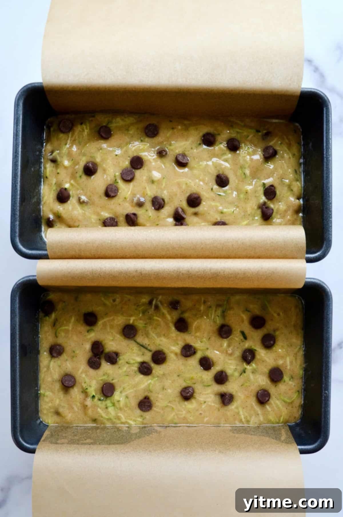 Two loaf pans lined with parchment paper filled with zucchini bread batter topped with chocolate chips.