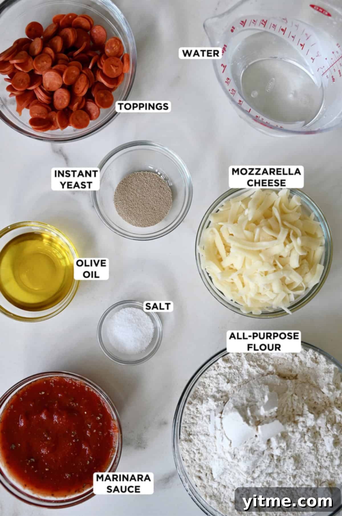 Various sizes of glass bowls containing all of the ingredients needed to make focaccia pizza, including mini pepperoni, water, instant yeast, mozzarella cheese, all-purpose flour, salt, marinara sauce and olive oil.