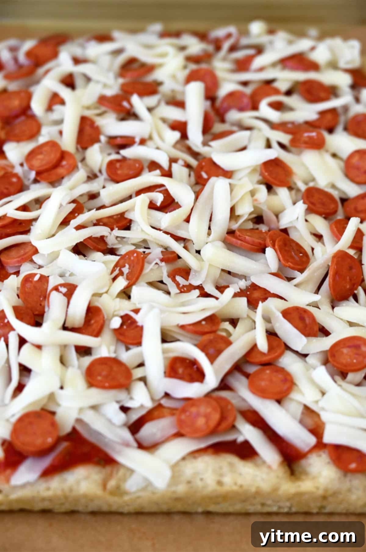 Shredded mozzarella and mini pepperoni atop a thick pizza dough.