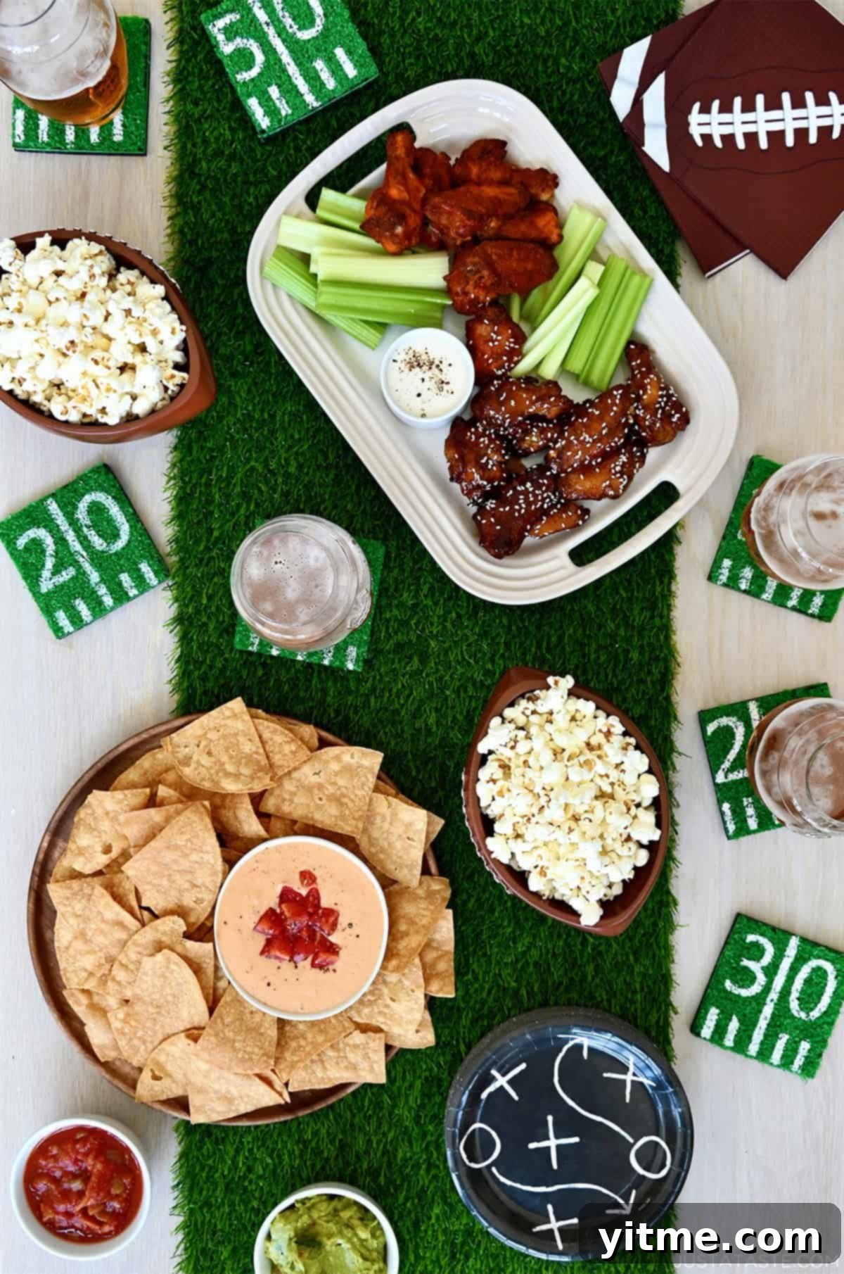 A top-down view of a tablescape with an astroturf runner and football snack foods