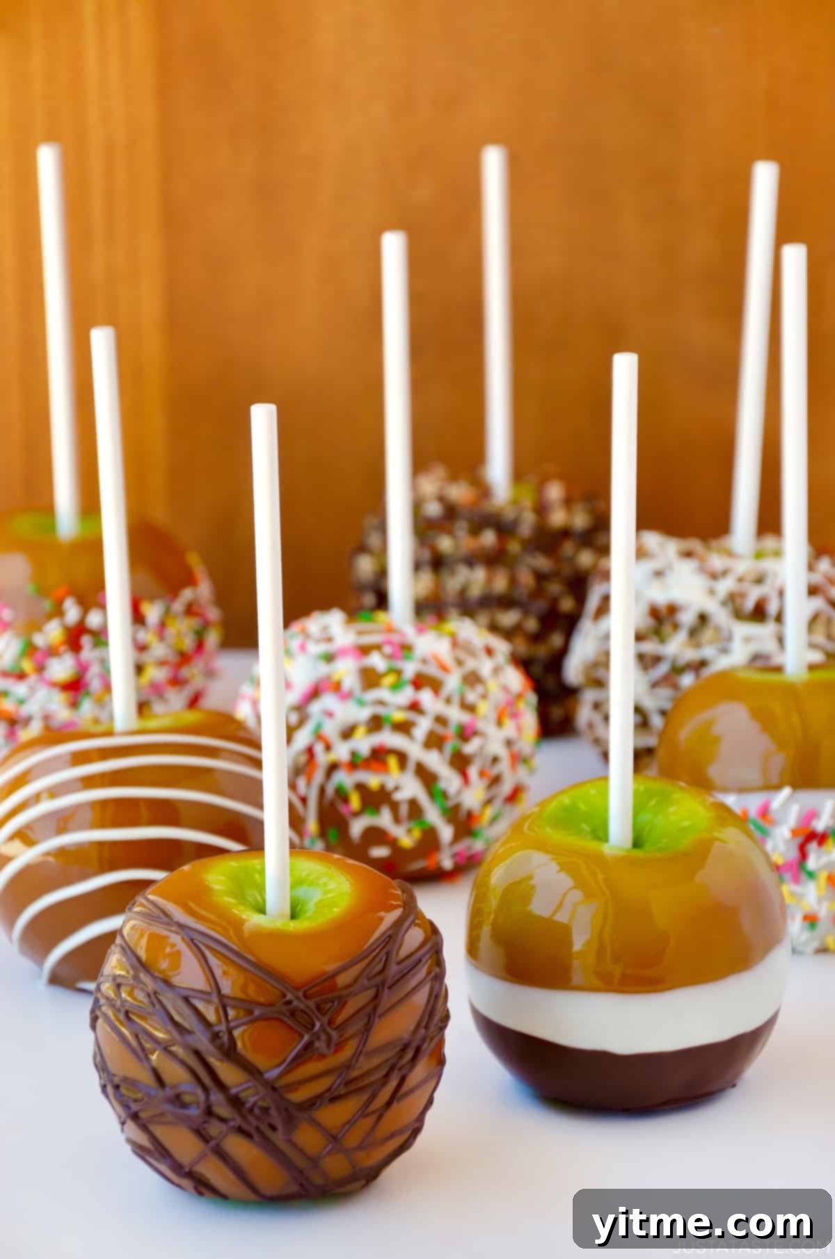 Caramel apples decorated with different toppings, including drizzled with milk chocolate, chopped walnuts, rainbow sprinkles and white chocolate.