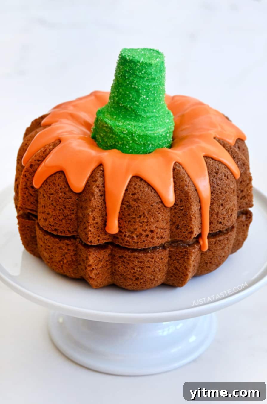 Easy Pumpkin Bundt Cake topped with a thick orange-colored glaze and a green sugar cone "stem" on a cake platter