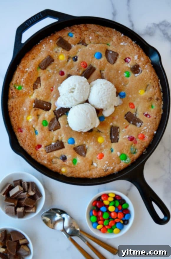 Leftover Halloween Candy Skillet Cookie topped with vanilla ice cream next to small bowls containing chocolate candy