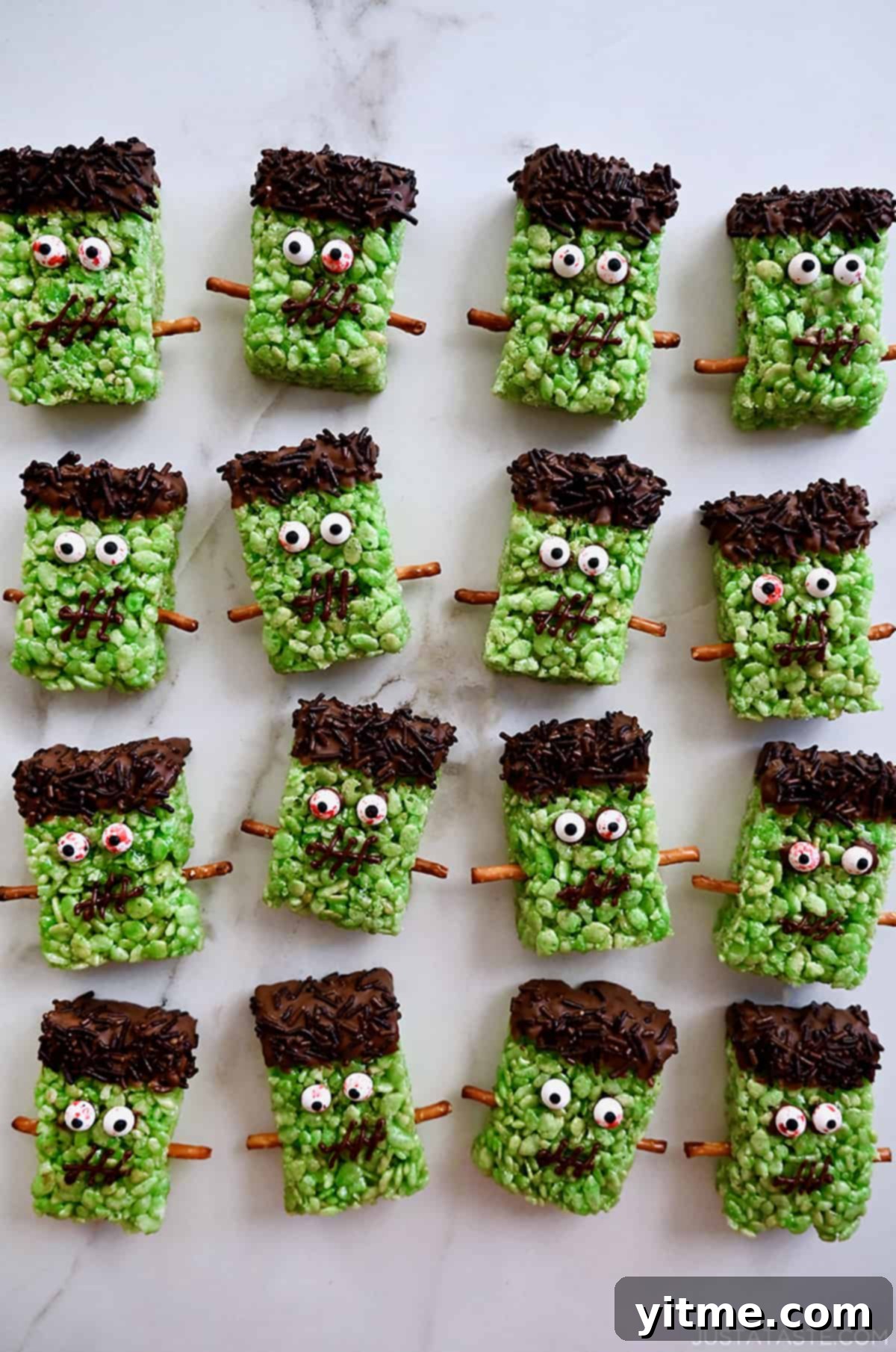 Four rows of Frankenstein Rice Krispie treats with candy eyes and pretzel stick bolts.