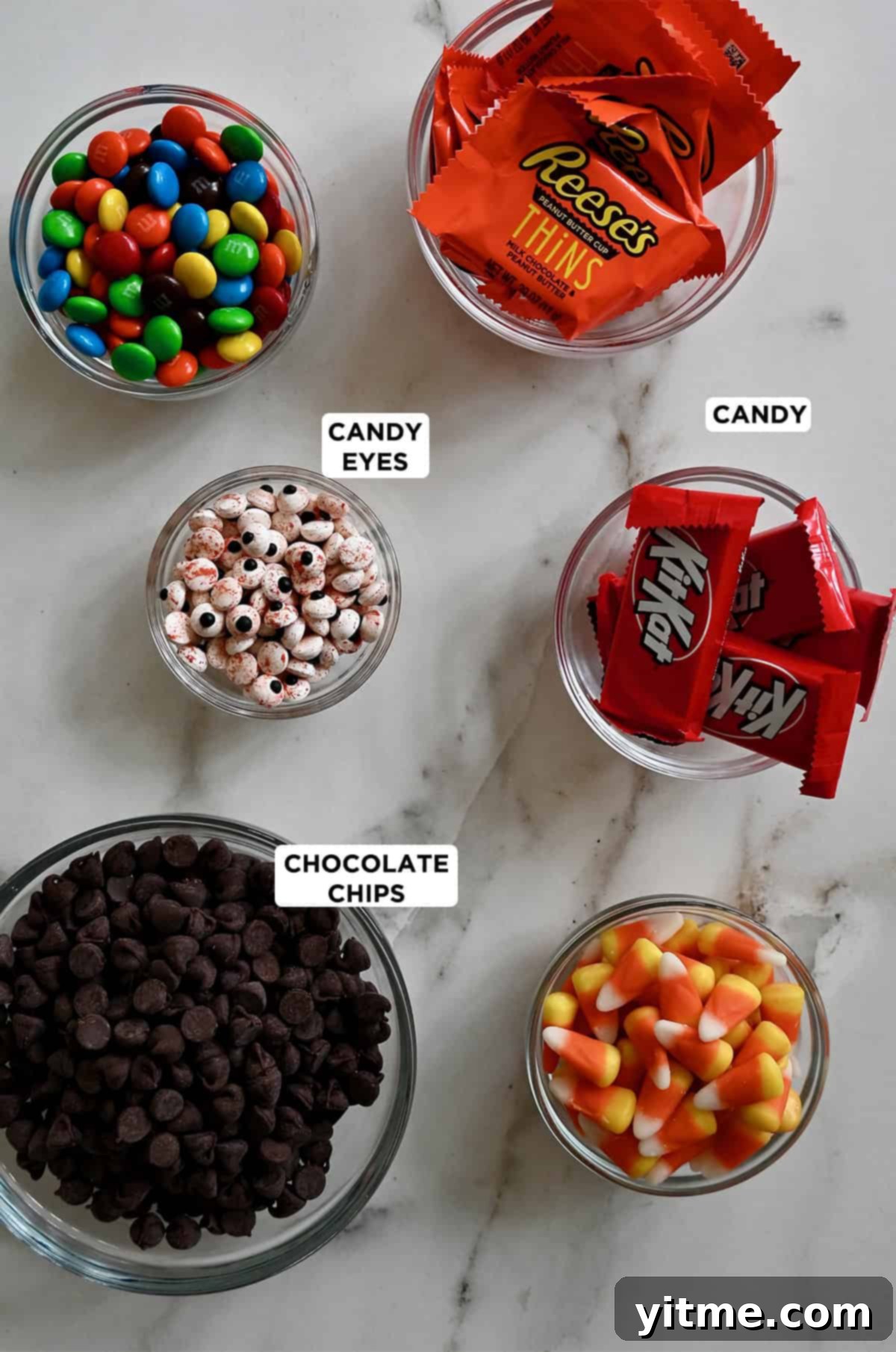 Ingredients to make Halloween chocolate candy bark, including high-quality chocolate, festive sprinkles, M&Ms, KitKat bars, candy corn, Reese's peanut butter bars and candy eyes.