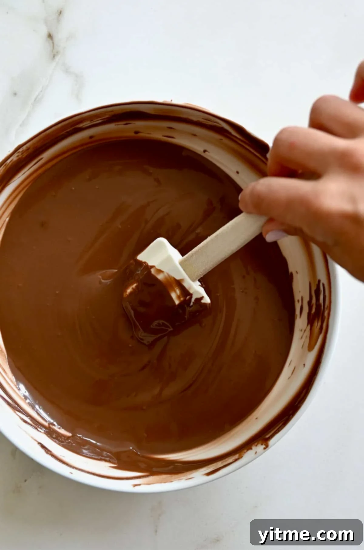 Melted chocolate in a glass bowl being stirred with a spatula.
