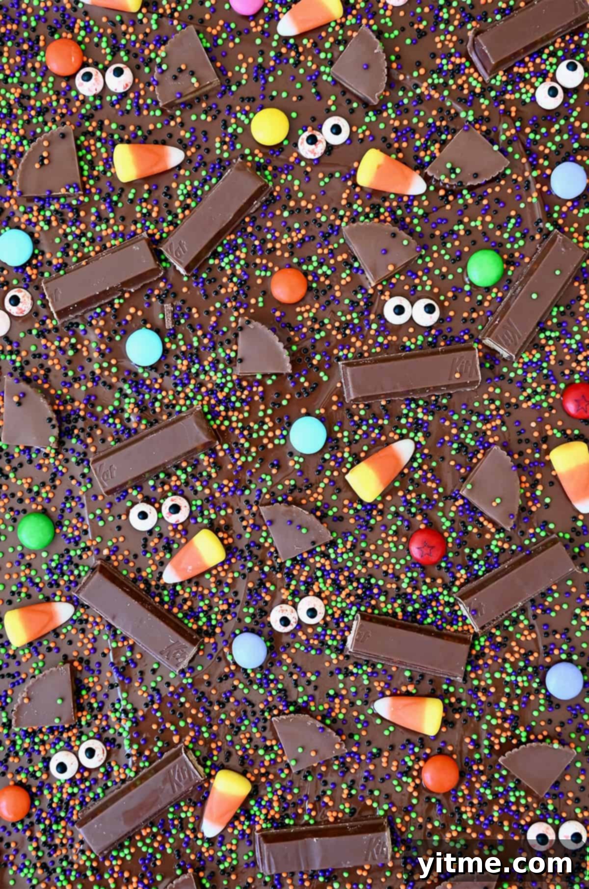 Halloween candy bark with festive sprinkles, M&Ms, candy corn, Reese's and KitKat bars before being broken into pieces.