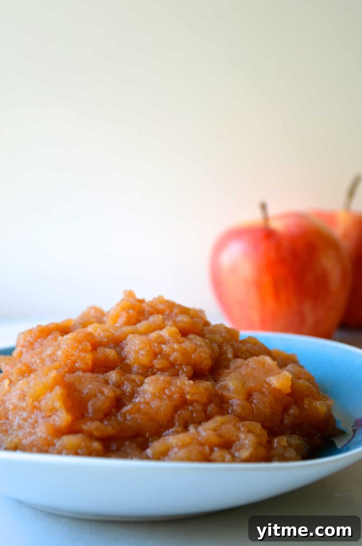 A bowl of homemade slow cooker applesauce with two apples in the background