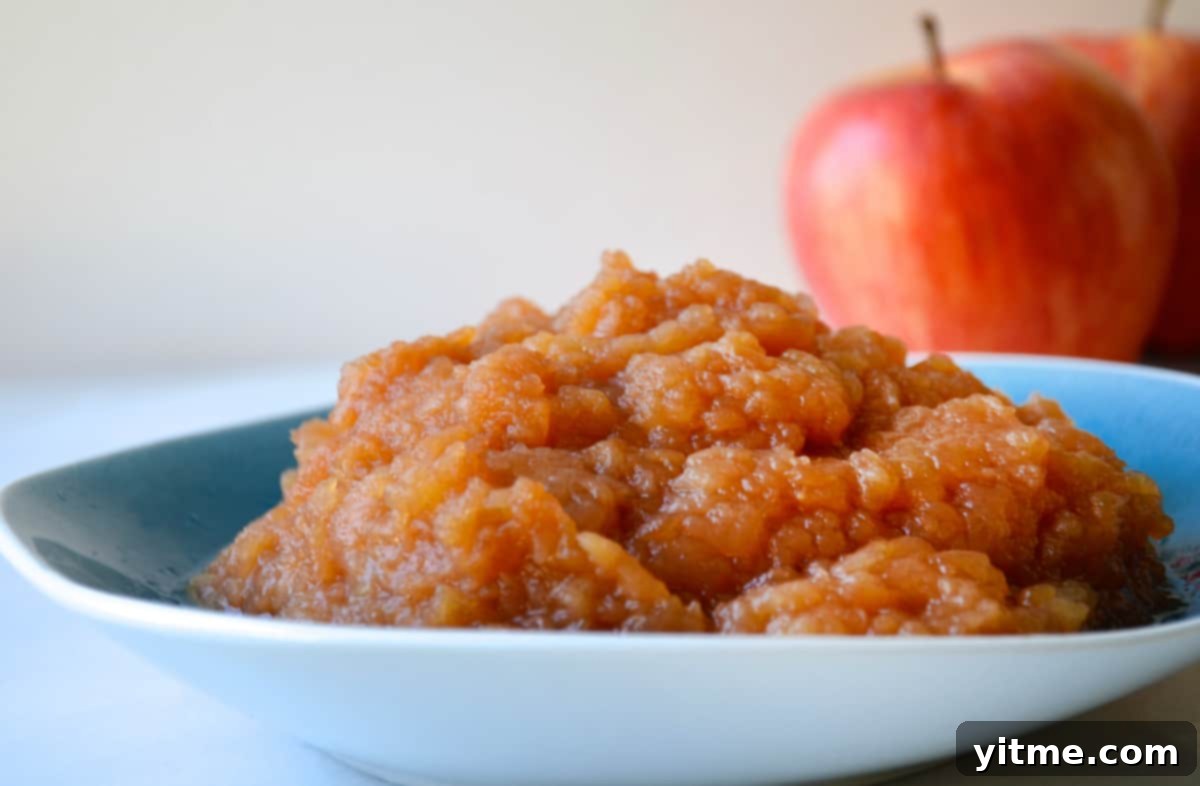 A blue bowl of slow cooker applesauce with apples in the background