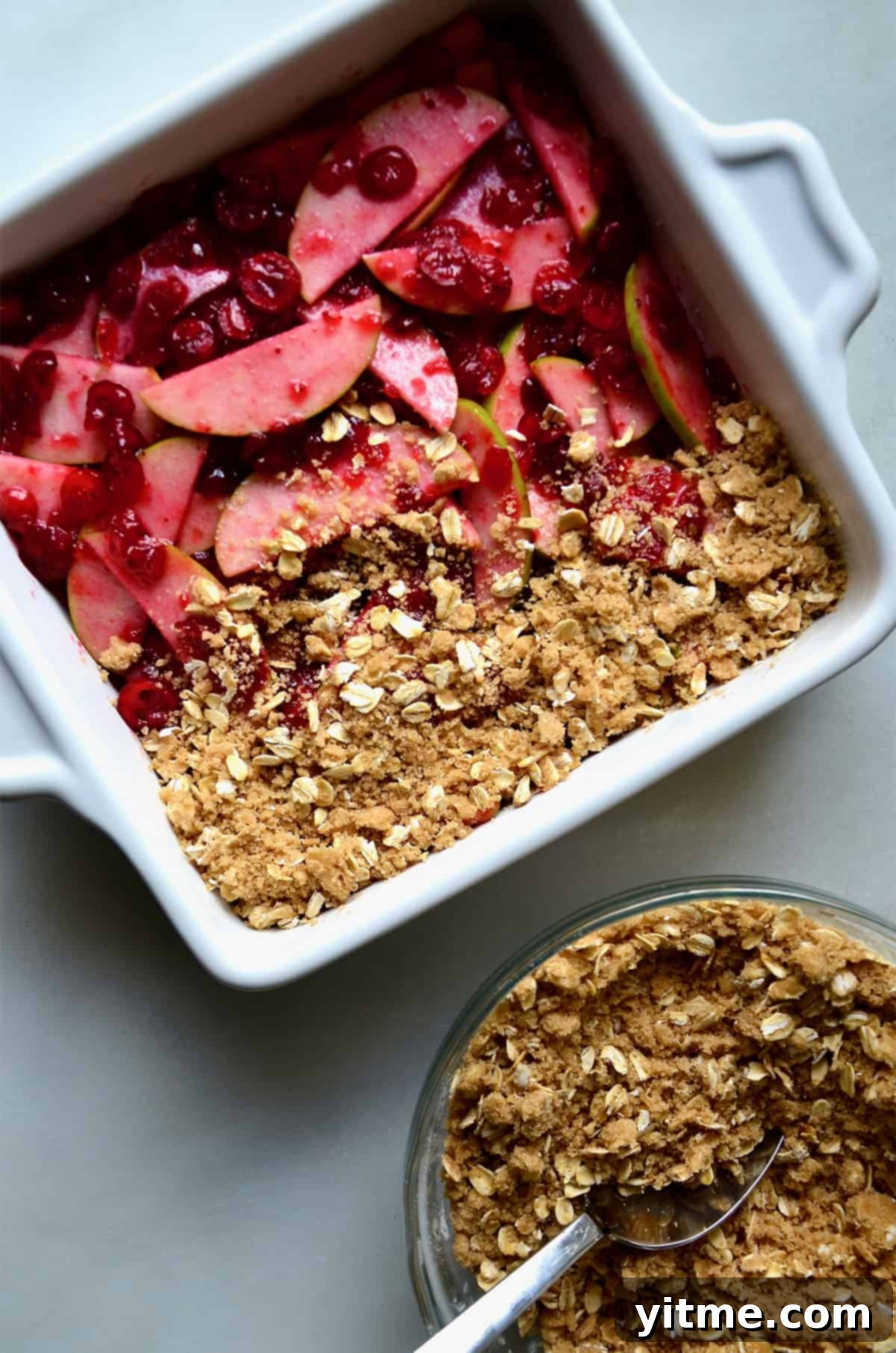 A square baking dish containing apple slices and cranberry sauce topped with oat crisp topping.