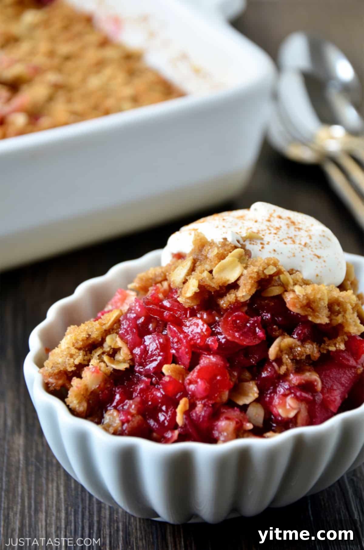 Cranberry apple crisp topped with whipped cream in an oval ramekin.