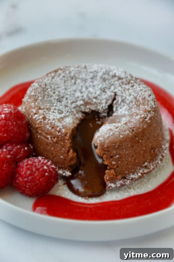 A decadent chocolate lava cake served on a pristine white plate, accompanied by a vibrant raspberry sauce and fresh raspberries.