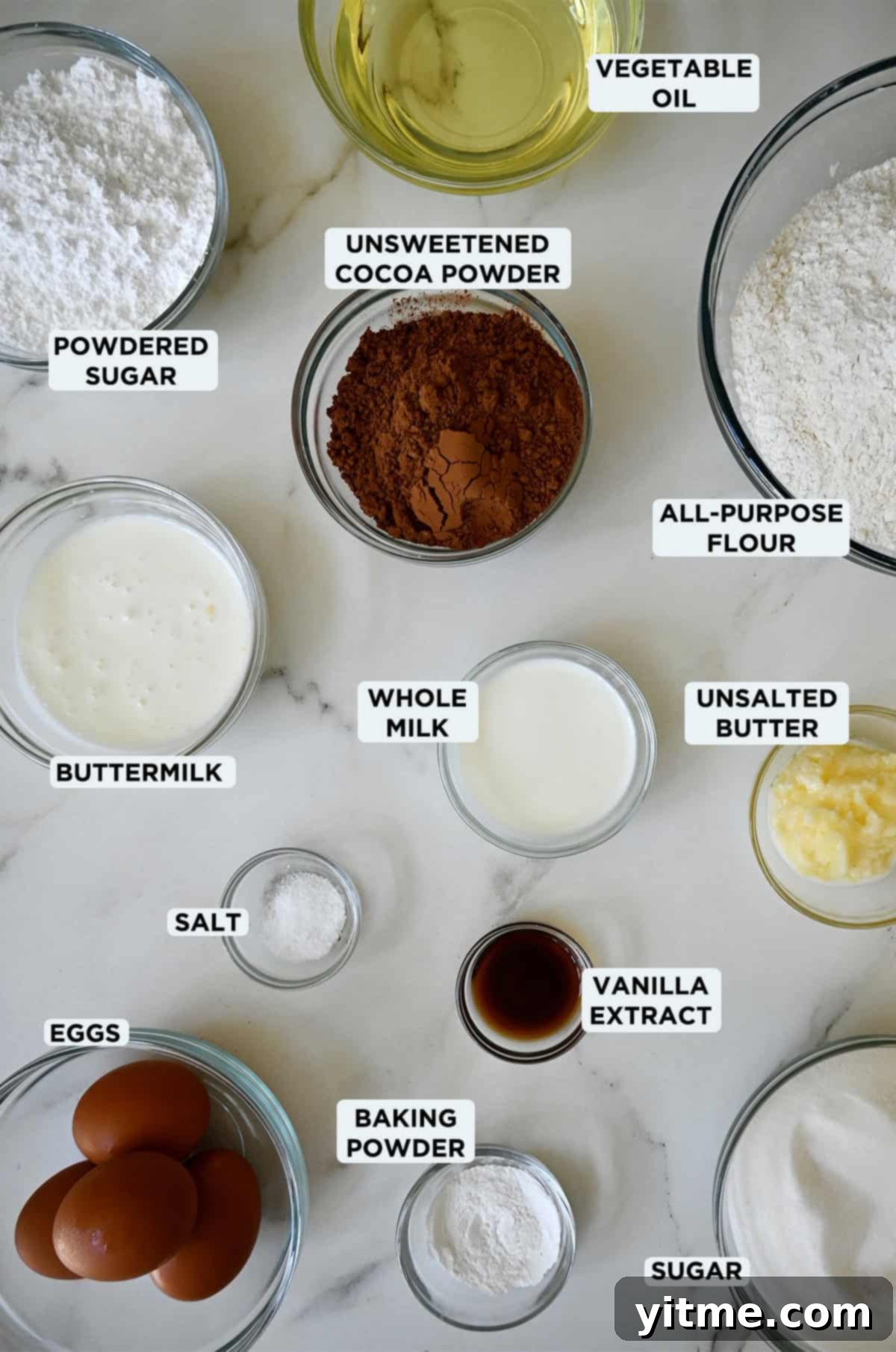 Various glass bowls holding the ingredients for chocolate doughnut holes and glaze, meticulously arranged on a rustic wooden surface.