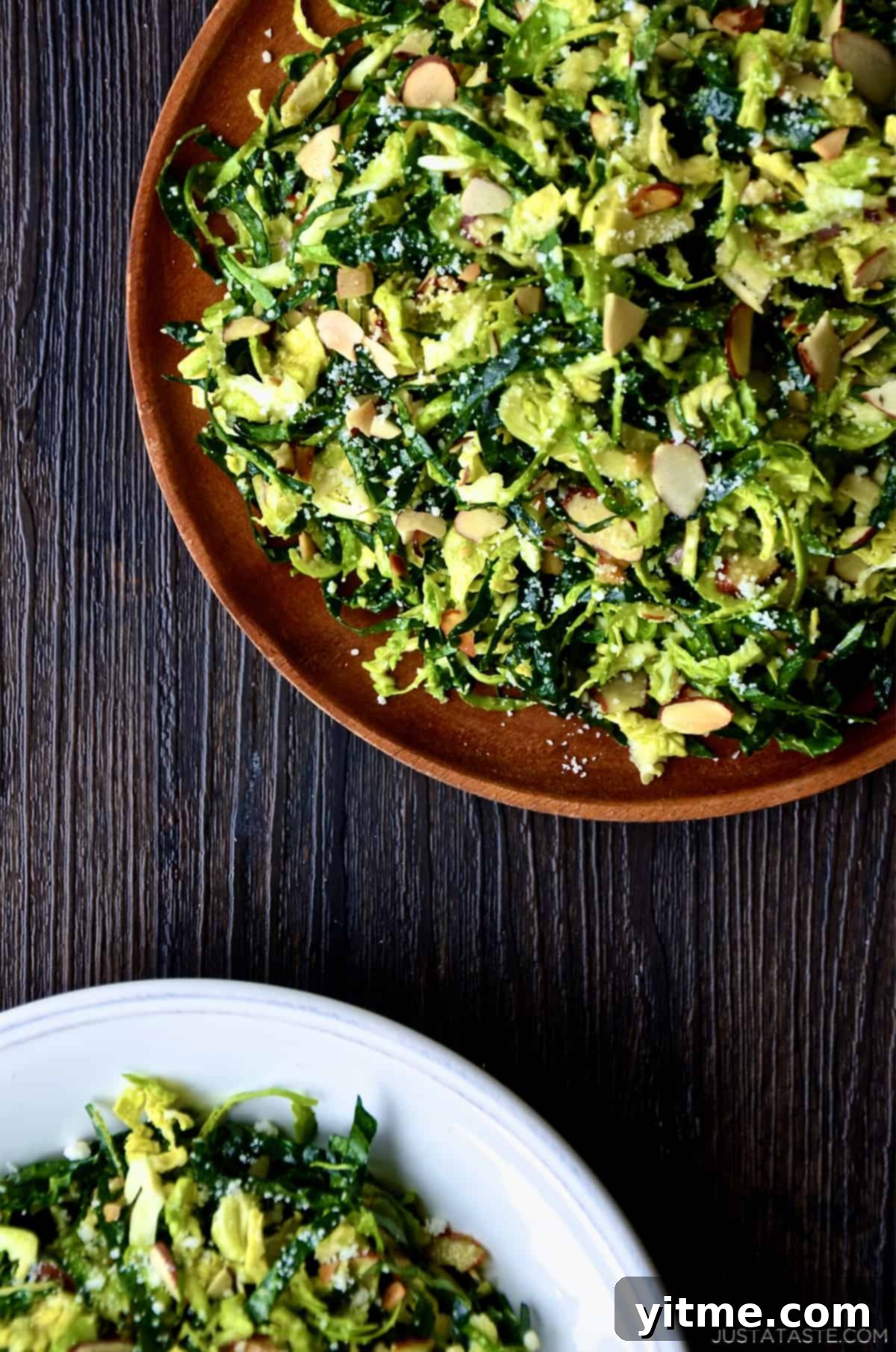 Two plates of shredded kale and Brussels sprouts salad with sliced almonds, topped with grated Parmesan cheese.