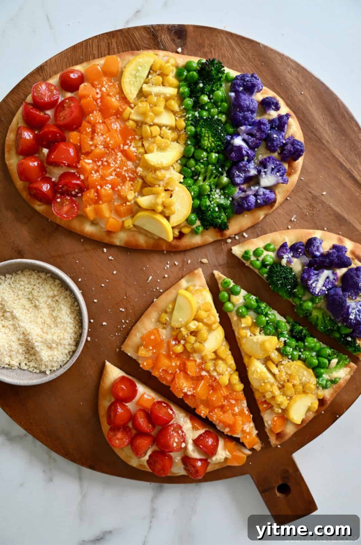 Two flatbread pizzas topped with a rainbow of veggies, including halved cherry tomatoes, diced orange bell pepper, fresh corn kernels, sliced summer squash, peas, broccoli florets, and purple cauliflower florets.