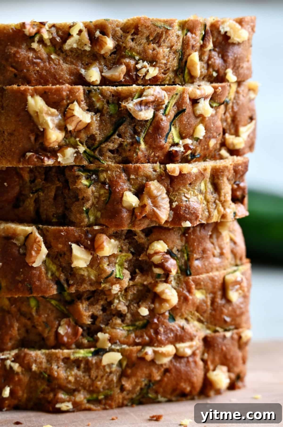 Slices of healthy zucchini bread with walnuts stacked six high on a cutting board.
