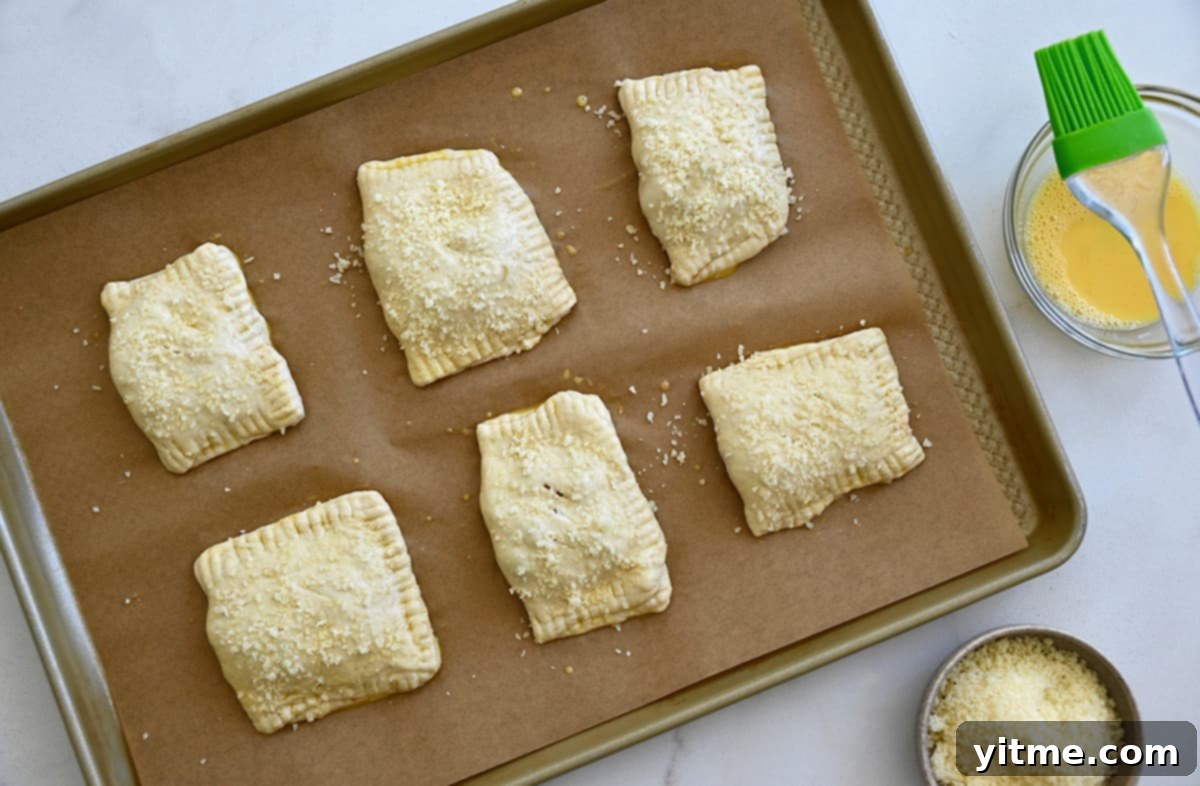 Unbaked homemade pizza pockets brushed with an egg wash and sprinkled with parmesan cheese on a baking sheet lined with parchment paper.