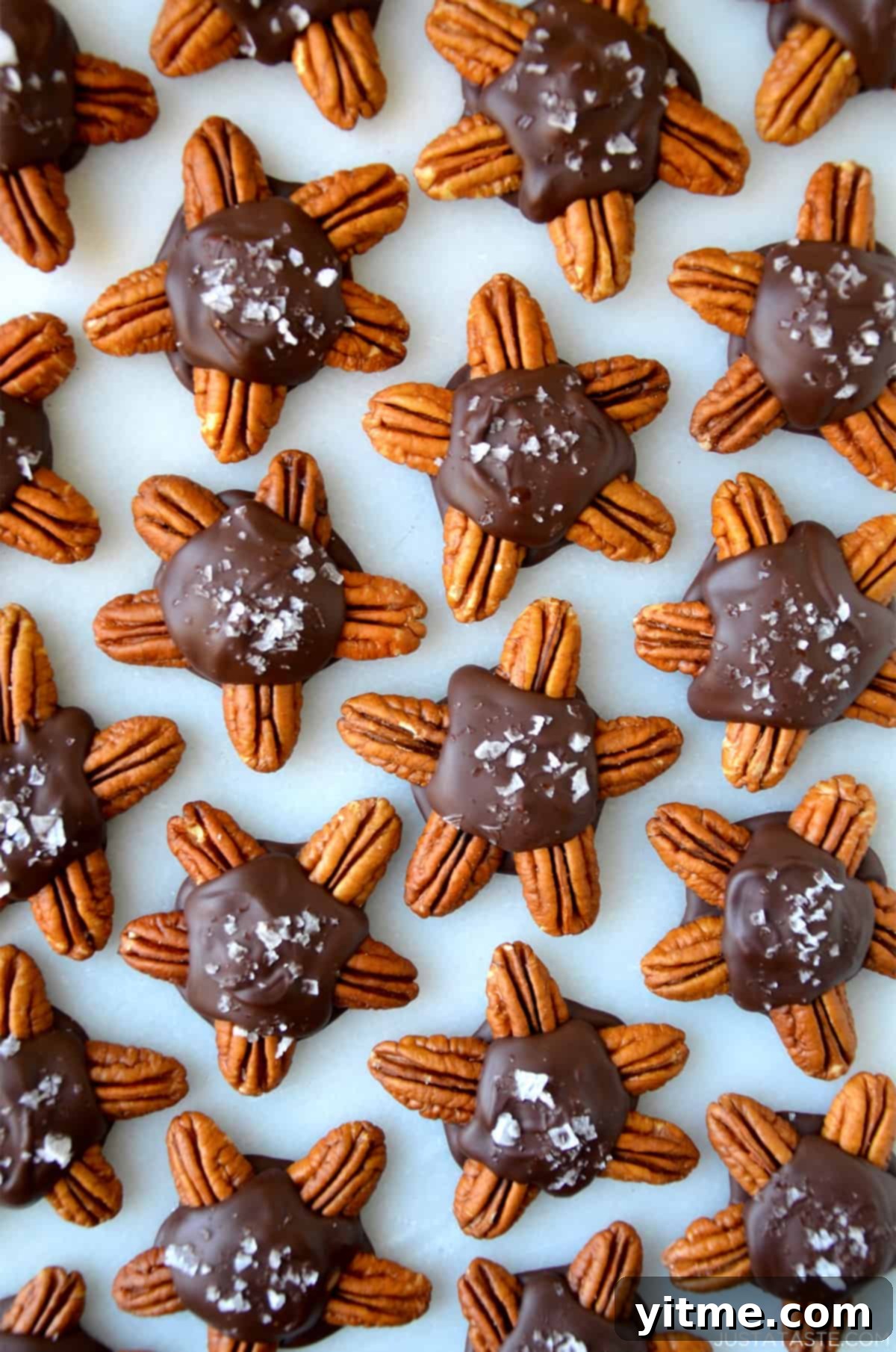Chocolate turtles topped with flakey salt on a parchment-lined baking sheet.