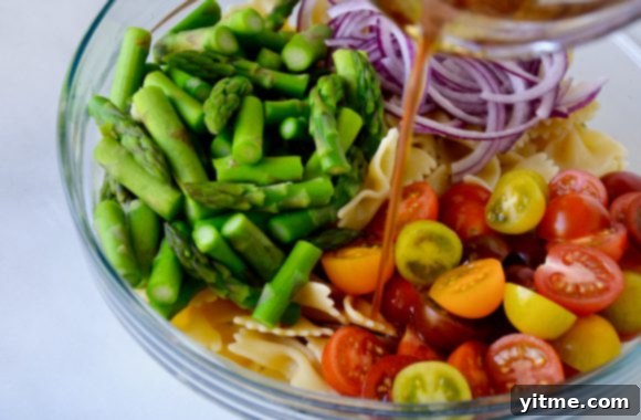 Asparagus Pasta Salad with Zesty Italian Vinaigrette 4 Dressing being poured over cherry tomatoes and asparagus in a clear bowl