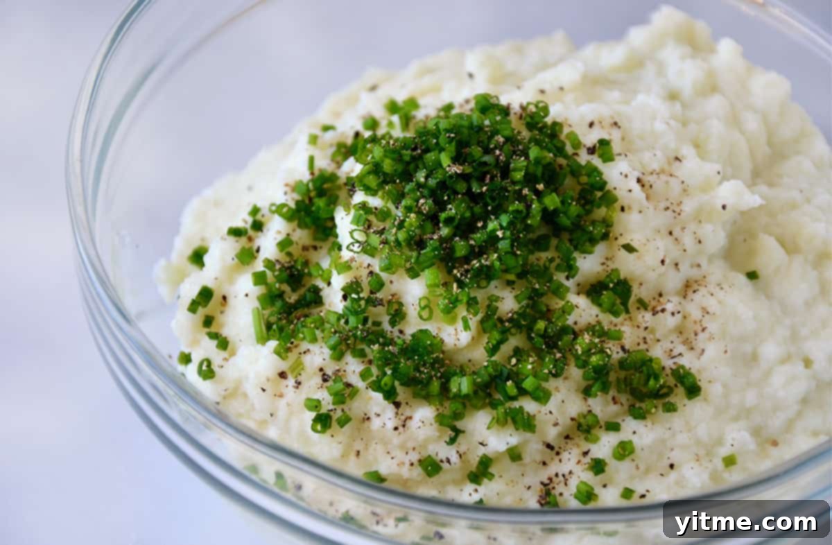 Cheesy Chive Mashed Cauliflower 7 Mashed cauliflower, minced chives and black pepper in a glass mixing bowl.