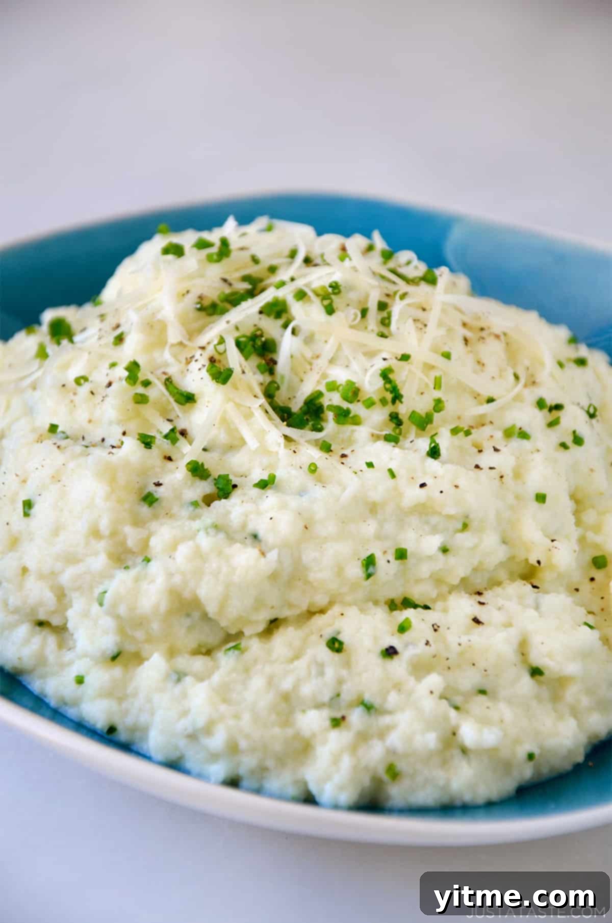 Cheesy Chive Mashed Cauliflower 8 Mashed cauliflower topped with grated cheese, minced chives and black pepper in a bowl.