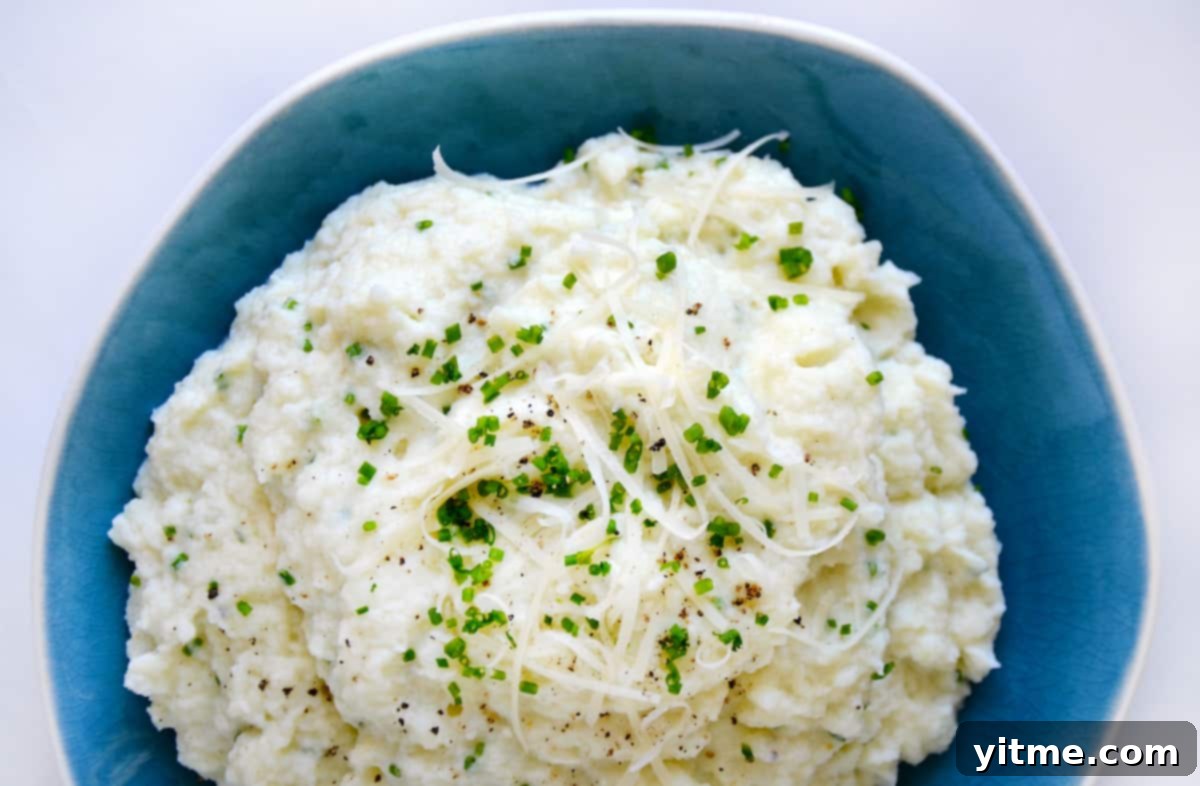 Cheesy Chive Mashed Cauliflower 9 Mashed cauliflower topped with grated cheese, minced chives and black pepper in a blue bowl.