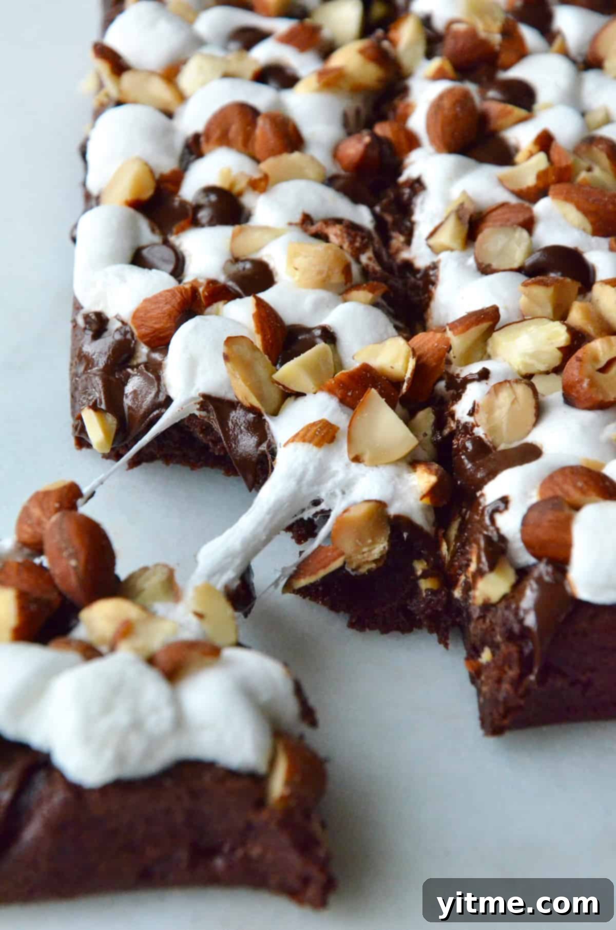 Rock road brownies topped with chopped almonds. A piece of brownie is pulled off the corner.