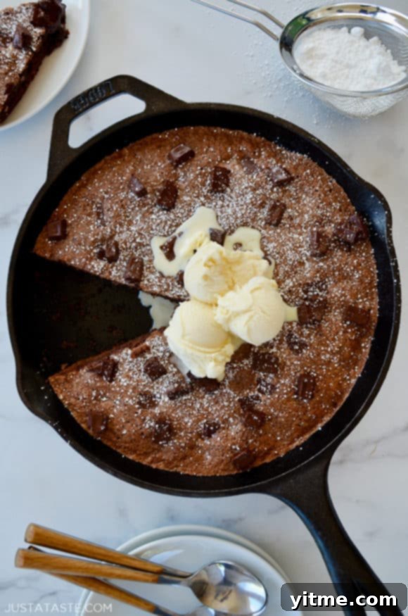 A cast-iron skillet brownie topped with ice cream and confectioners' sugar