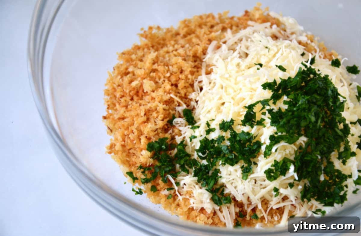 A glass mixing bowl containing freshly toasted breadcrumbs, grated Parmesan cheese, and vibrant chopped parsley, ready to be combined.