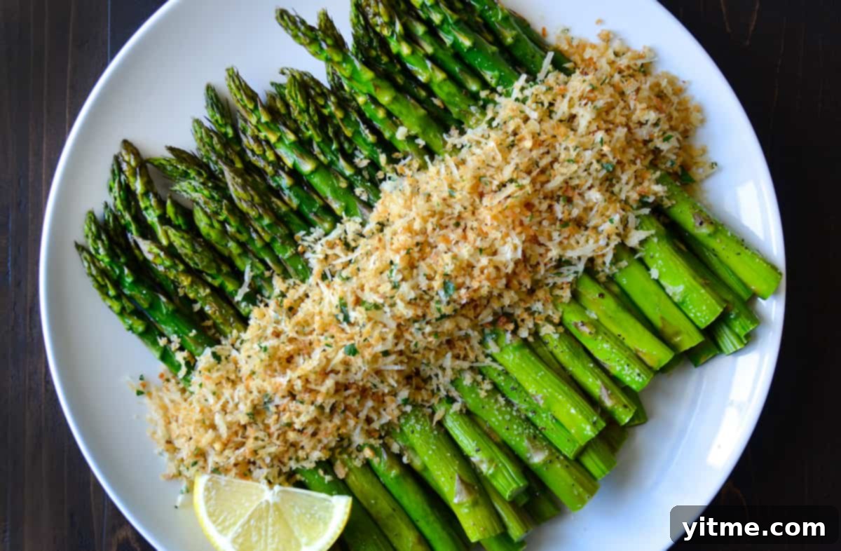Close-up of roasted asparagus topped with cheesy, herby toasted breadcrumbs on a white, round serving plate, ready to be enjoyed.