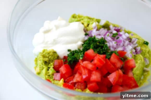Close-up of a spoon scooping creamy Greek Yogurt Guacamole, highlighting its smooth texture and fresh ingredients.