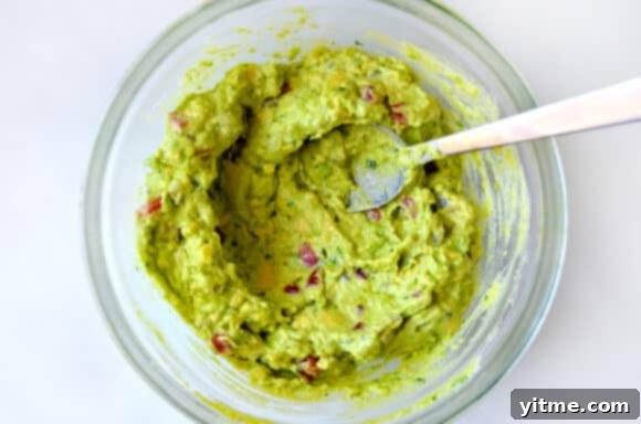 A serving of Creamy Greek Yogurt Guacamole with a spoon, ready to be enjoyed.