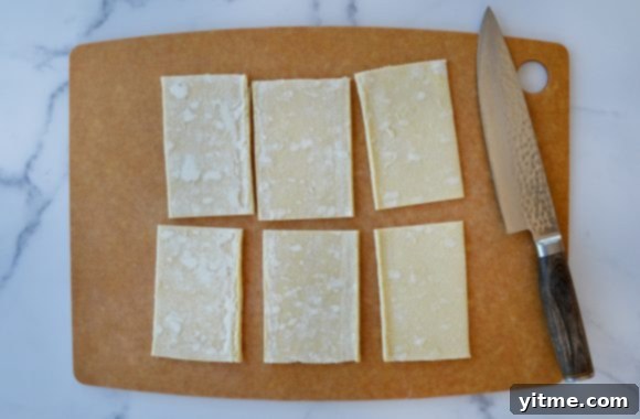 Cutting board containing six rectangles of cut puff pastry next to a sharp knife 